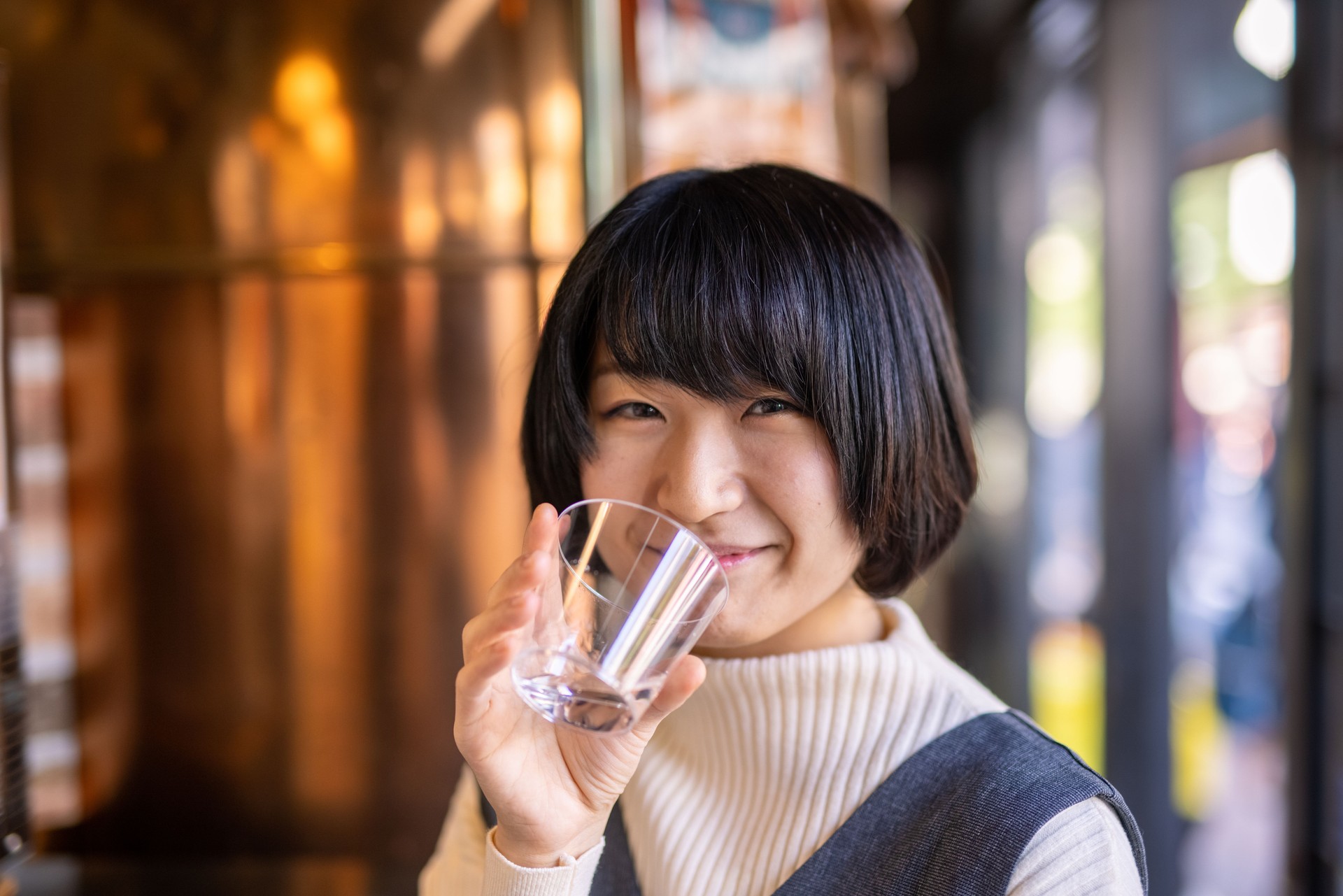 Happy young woman drinking a glass of 'saki' (Japanese rice wine) in liquor store