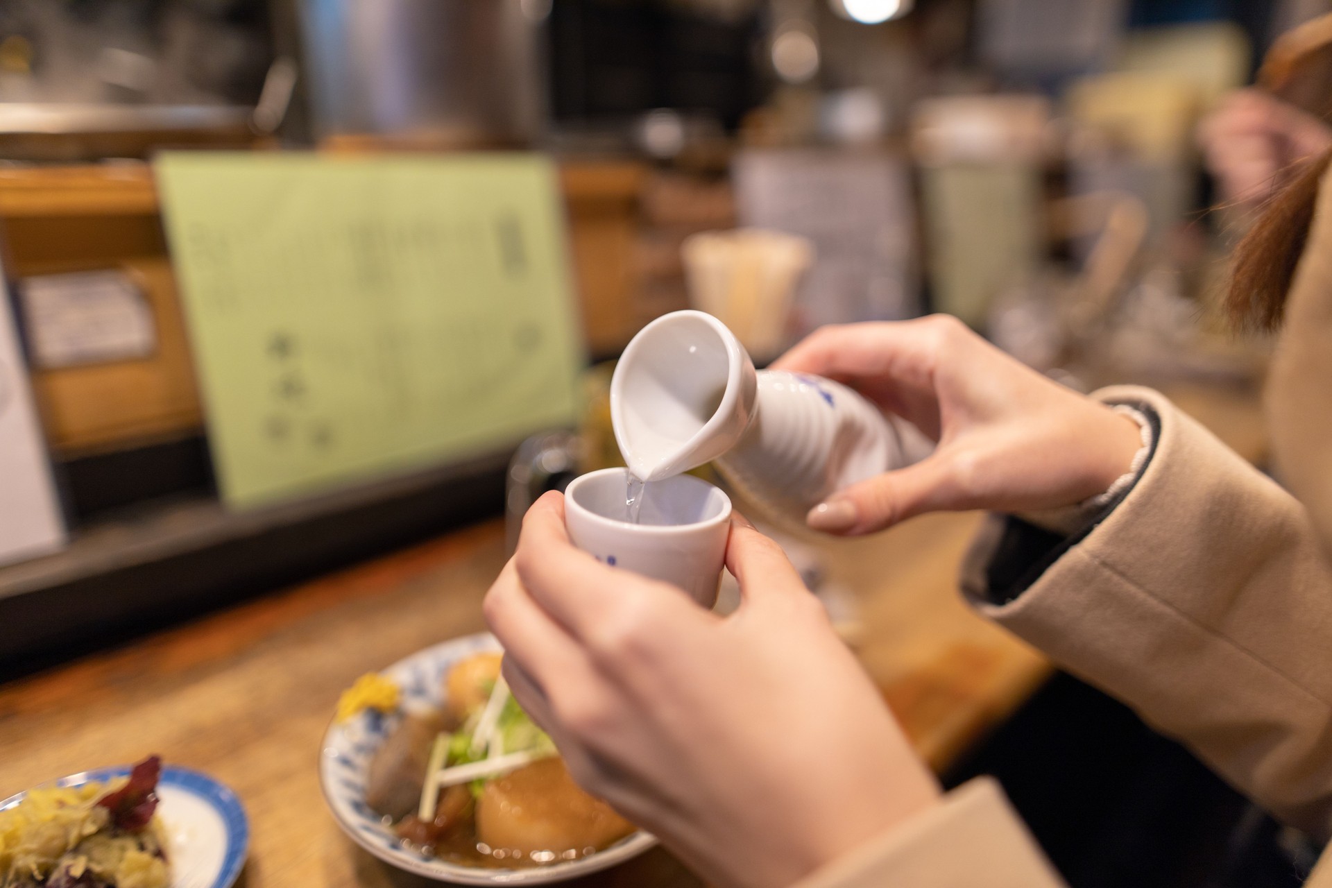 Young woman drinking Japanese Saki at Izakaya bar counter